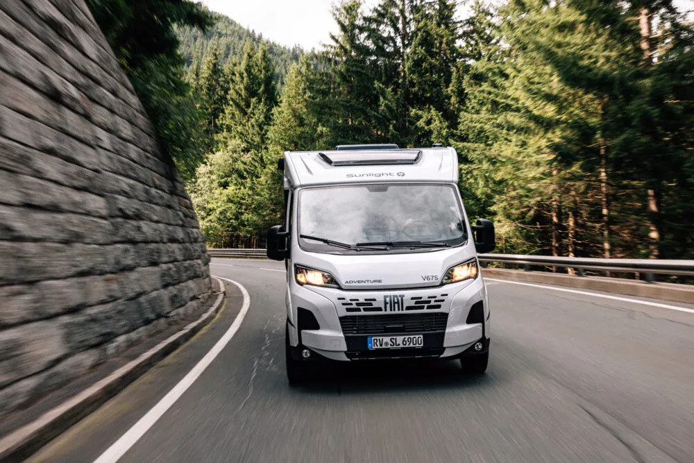 Ein Fiat Sunlight Adventure V67S Wohnmobil fährt auf einer kurvigen Straße durch einen Wald.