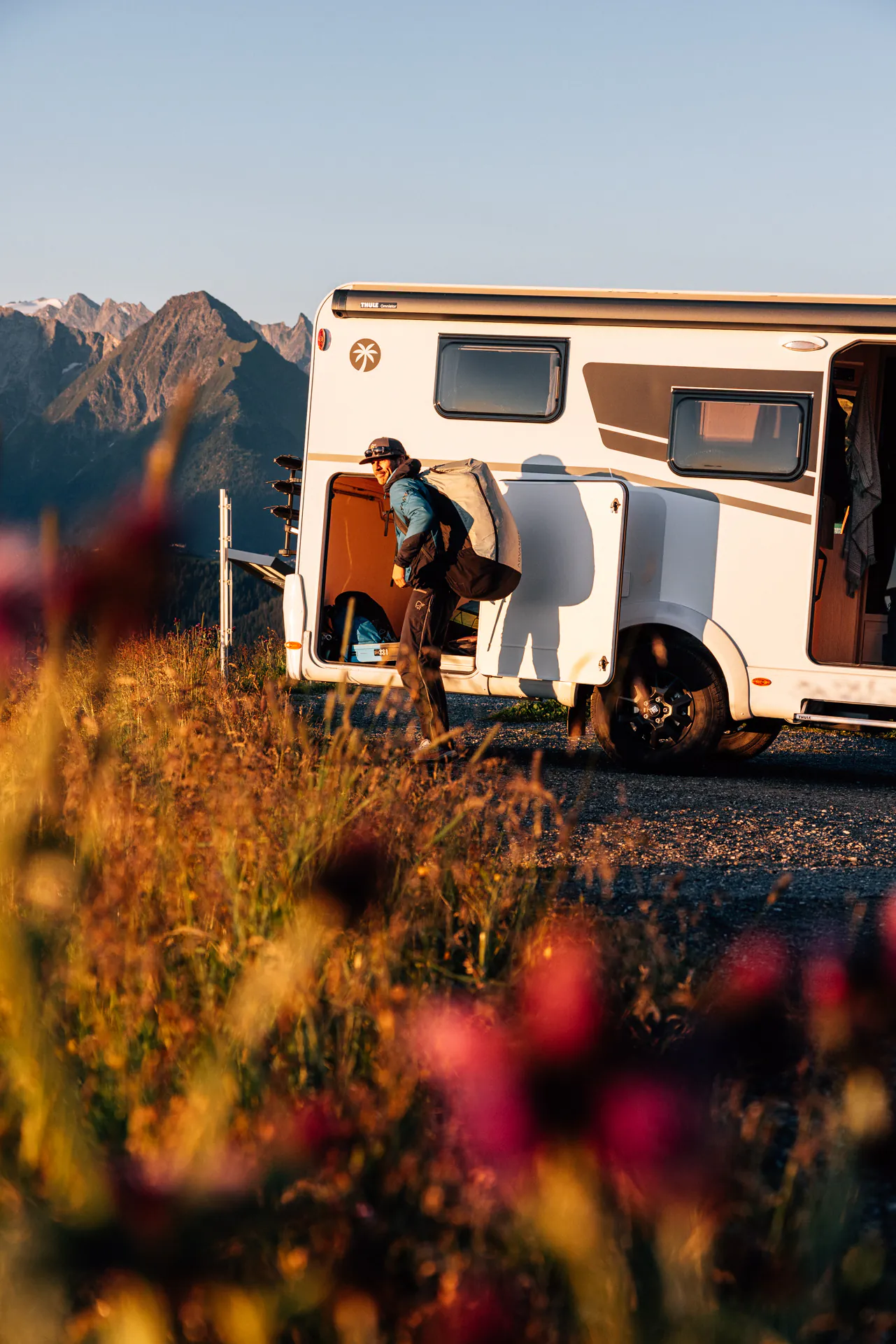 Person mit Rucksack neben einem Wohnmobil in Berglandschaft.