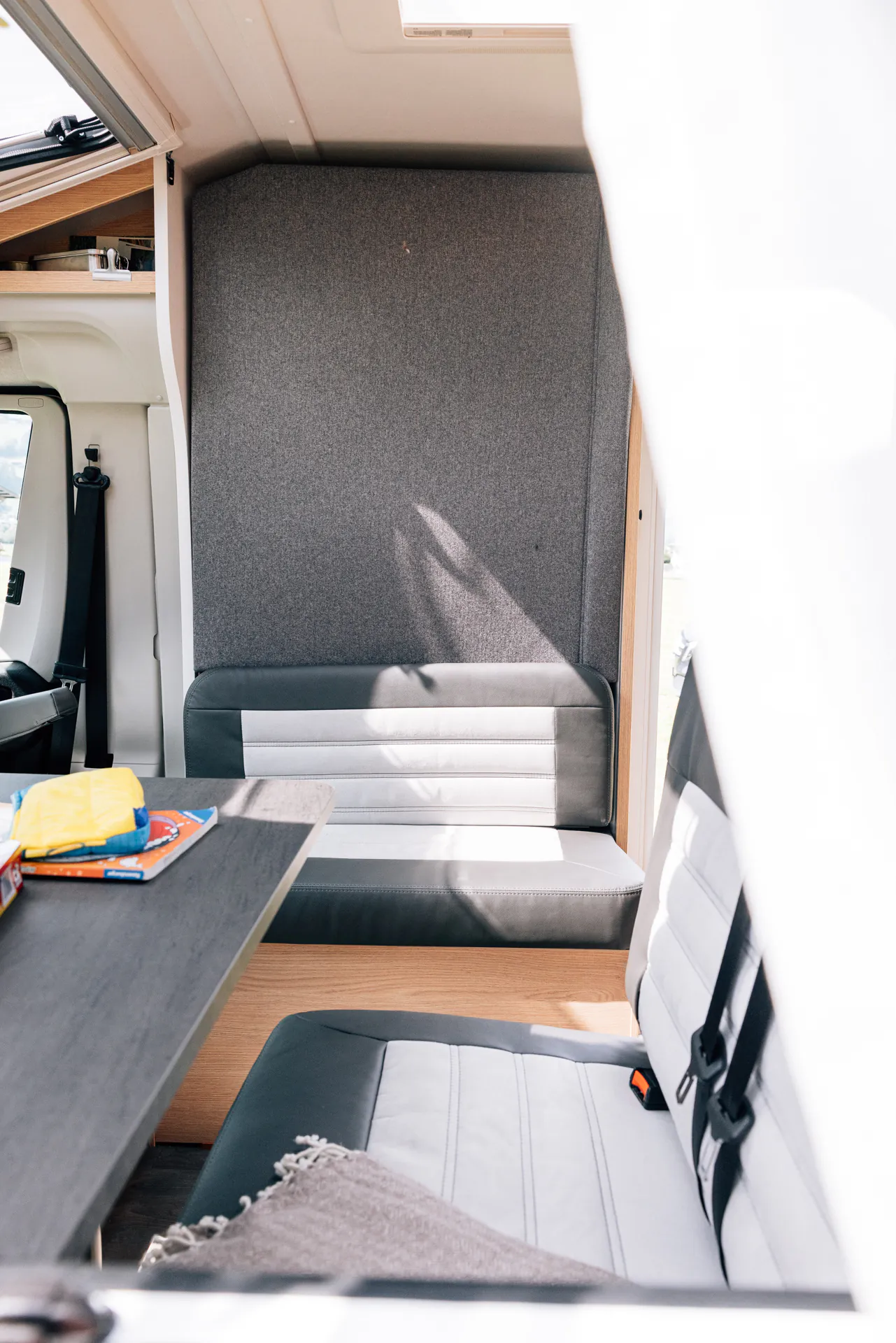 Innenansicht eines Wohnmobils mit grauen und weißen Sitzen sowie einem Tisch.