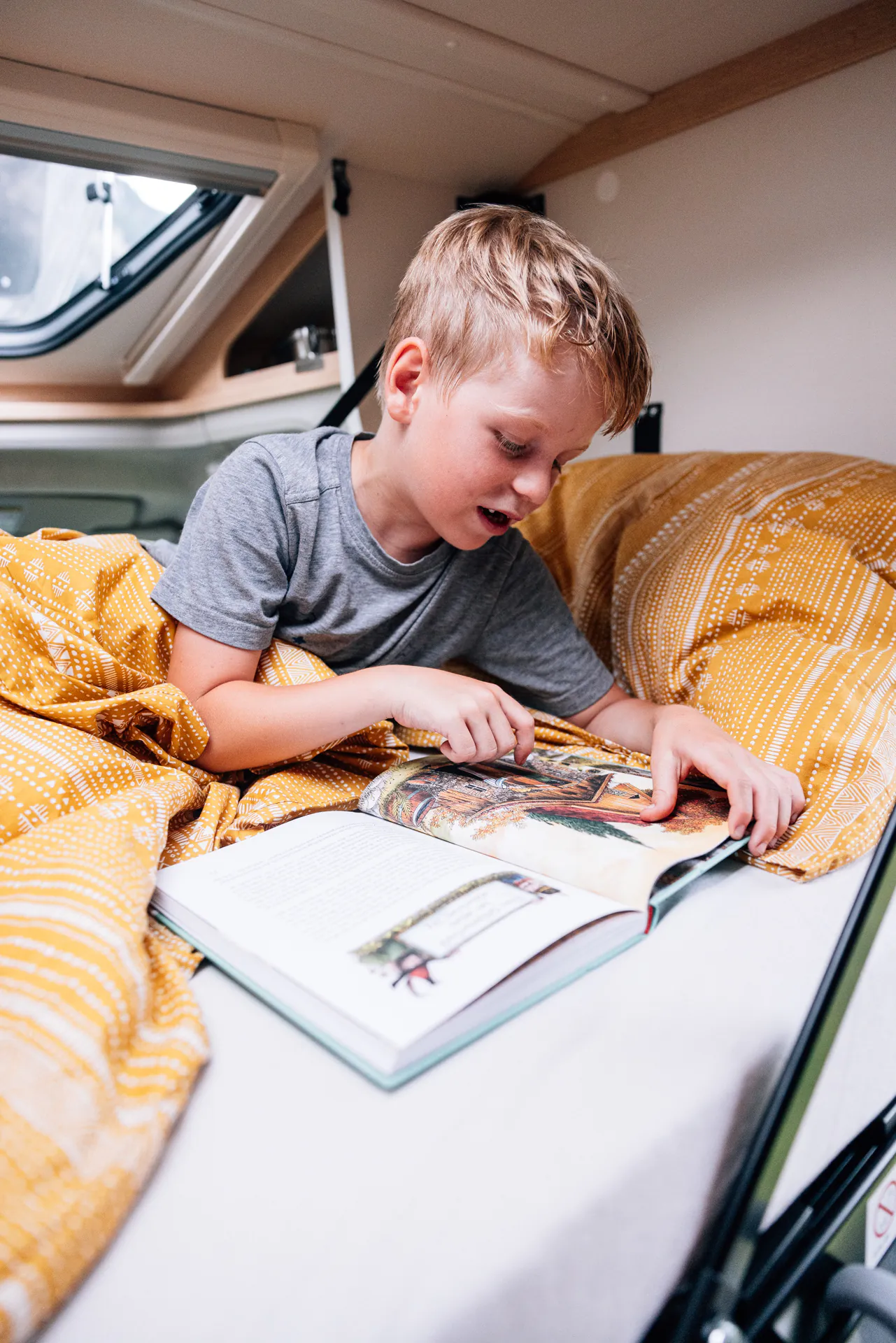 Ein Kind liest ein Buch in einem Camperbett.