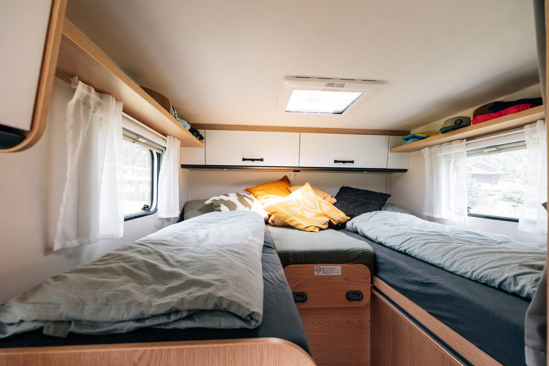 Innenraum eines Wohnmobils mit zwei Einzelbetten, Decken und Kissen.