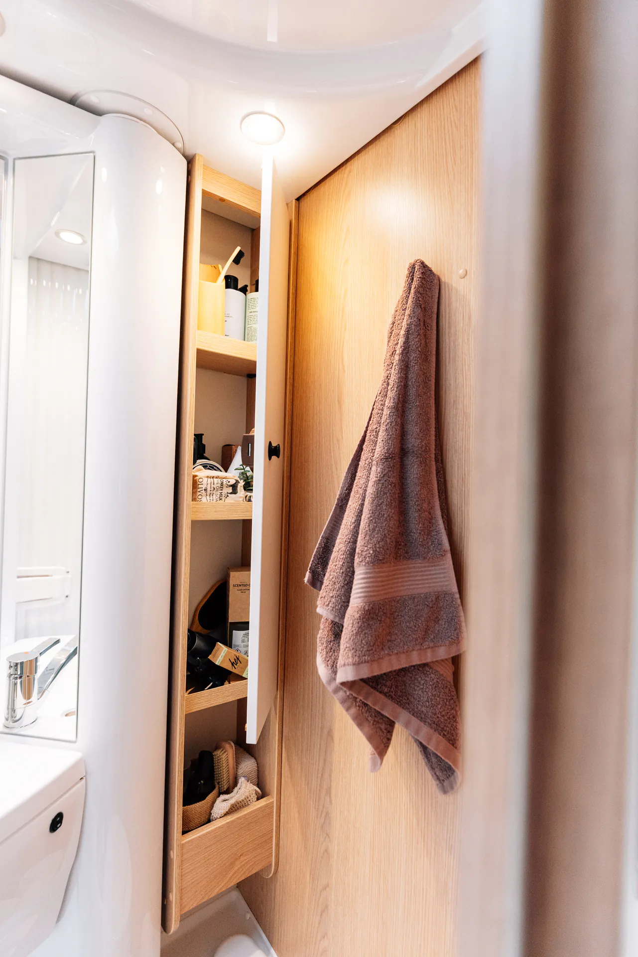 Offener Badezimmerschrank in einem Wohnmobil mit Handtuch und Pflegeprodukten.