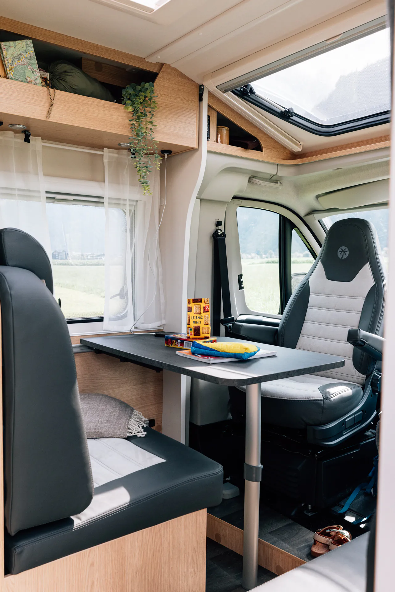 Innenraum eines Wohnmobils mit Tisch, Sitzbank und Fahrersitz, darauf Snacks und Spiele.
