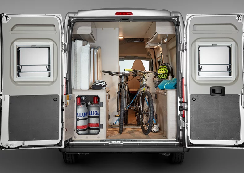 Ein geöffneter Camper zeigt zwei Fahrräder und Campingausrüstung im Laderaum.