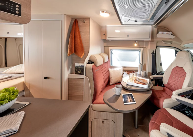Innenraum eines Campeo Wohnmobils mit Sitzgruppe, Tisch und Küchenzeile.