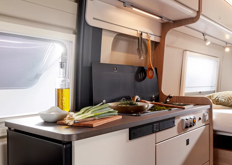 Innenansicht einer Camper-Küche mit Herd, Gewürzen und frischen Zutaten.