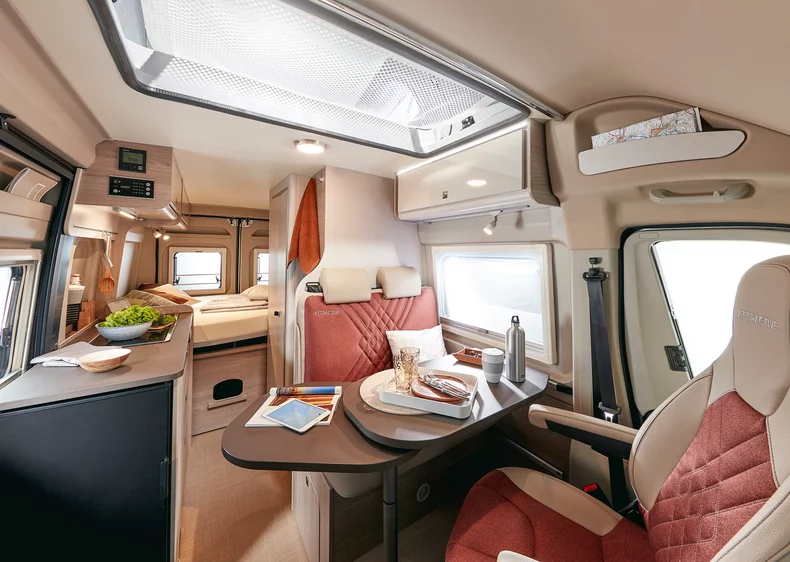 Innenansicht eines modernen Wohnmobils mit Essbereich, Küche und Schlafbereich.