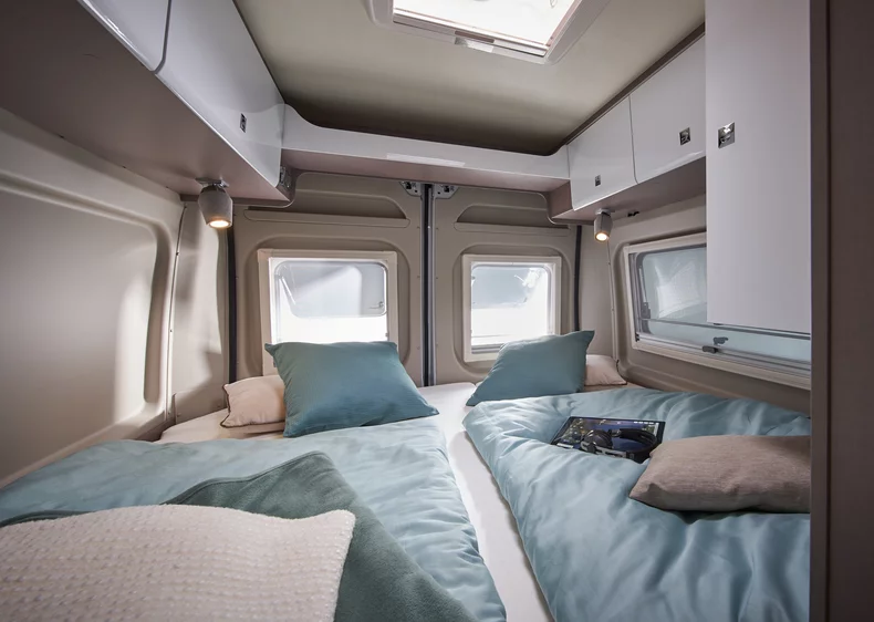 Innenraum eines Wohnmobils mit zwei Betten und Fenstern.