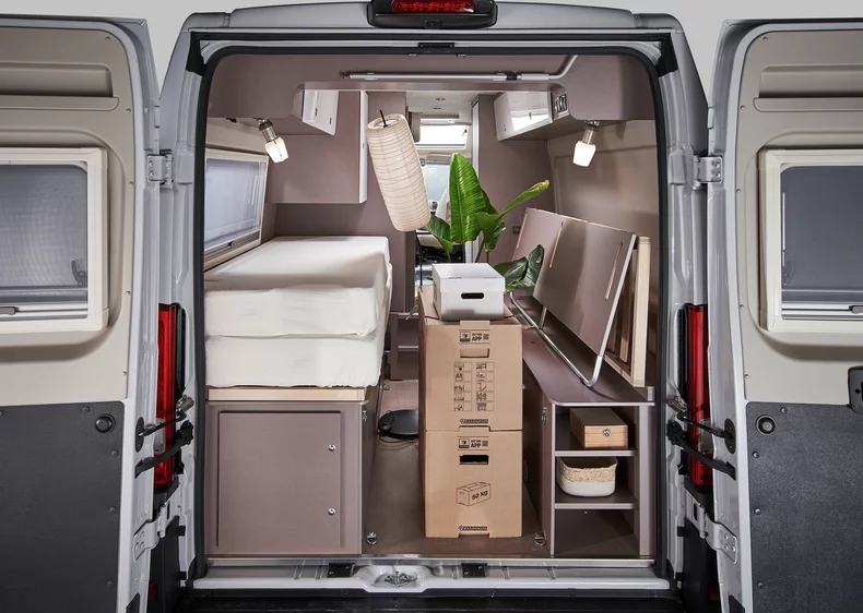 Innenansicht eines Camper-Vans mit Bett, Schränken und Pflanzen.