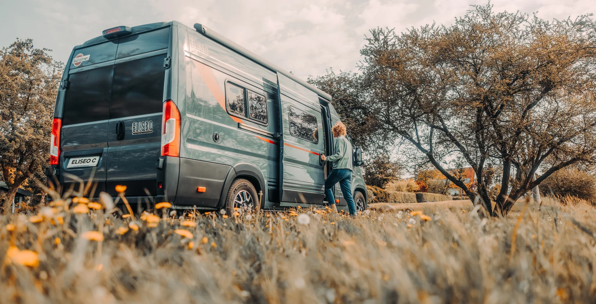 Eine Person steigt in einen Bürstner Eliseo C Campervan auf einer Wiese ein.