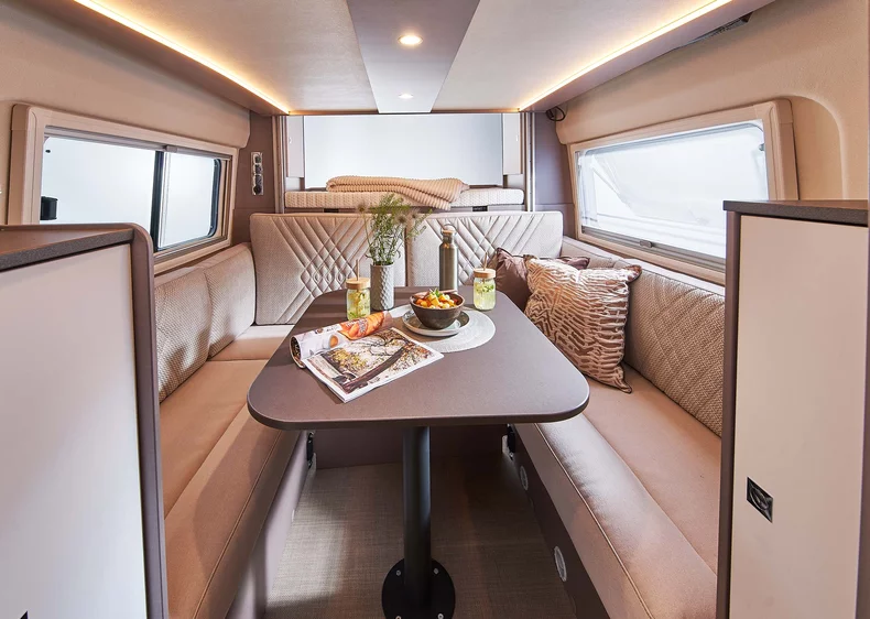 Innenansicht eines Campervans mit gemütlicher Sitzgruppe und gedecktem Tisch.