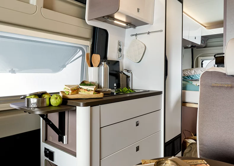 Innenraum eines Bürstner Eliseo Wohnmobils mit Küchenzeile, Sandwiches und Obst auf der Arbeitsfläche.