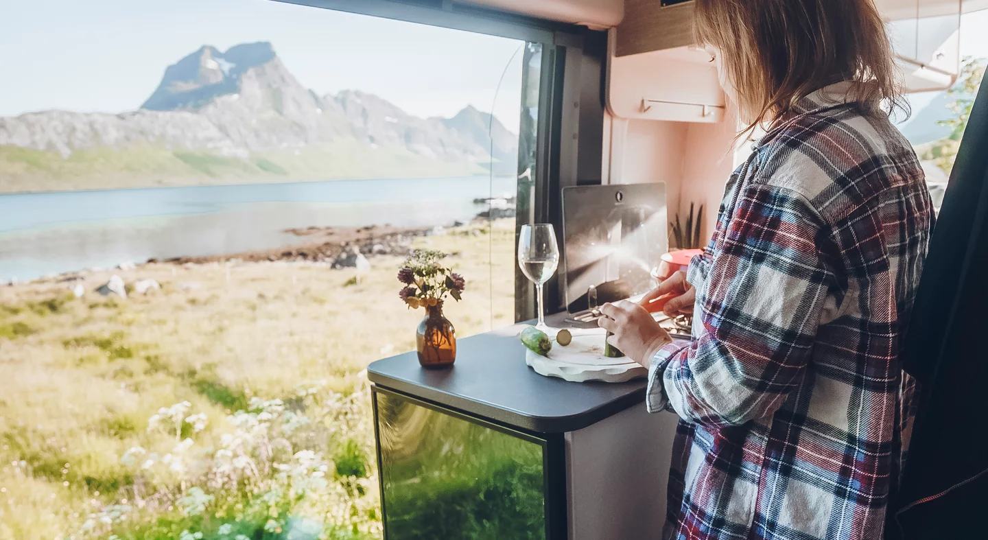 Eine Person schneidet Gemüse in einem Wohnmobil mit Blick auf eine Berglandschaft.