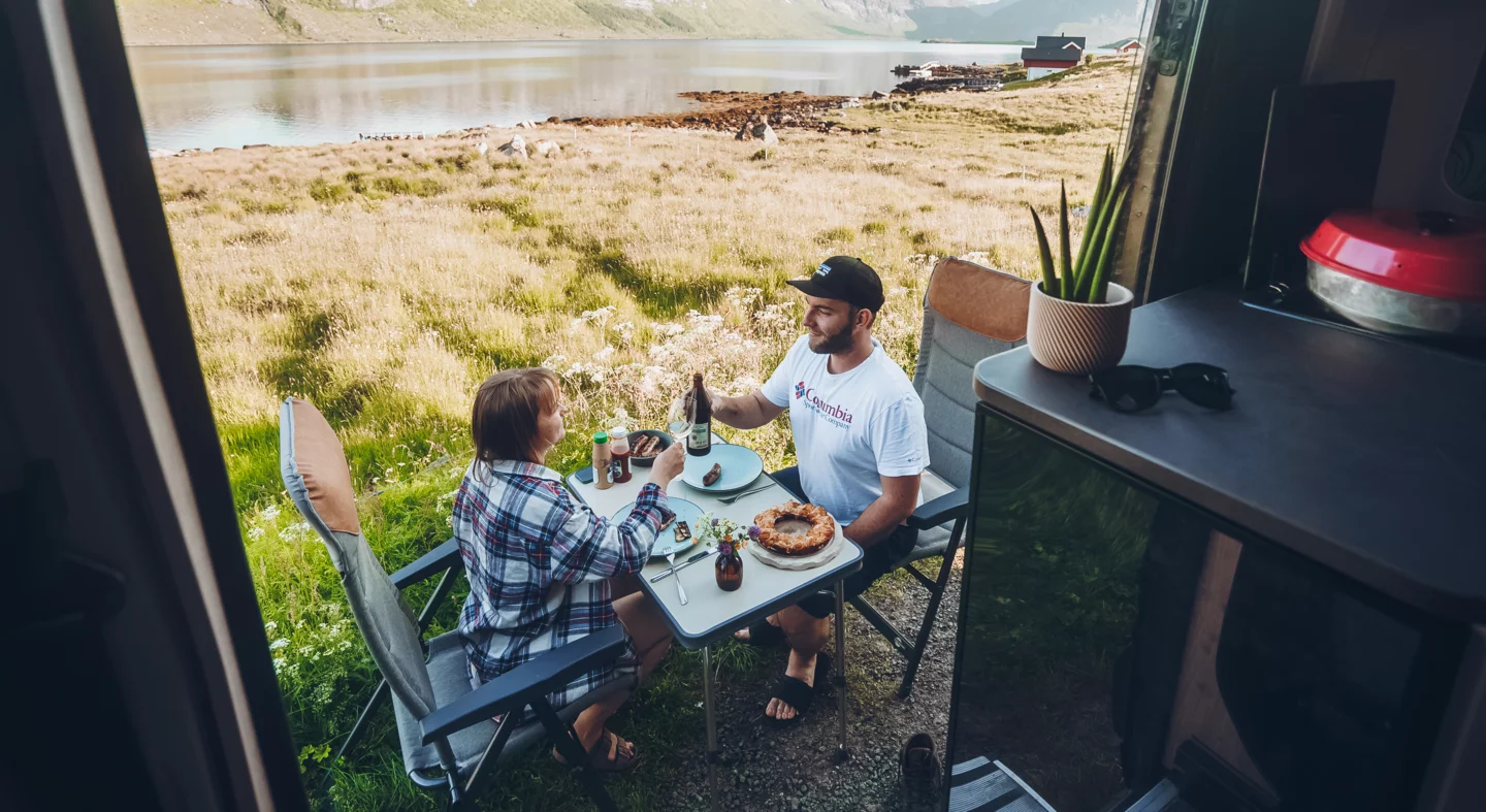Ein Paar sitzt draußen an einem Tisch und genießt eine Mahlzeit mit Blick auf eine malerische Landschaft.