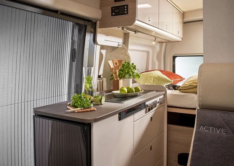 Innenansicht eines Wohnmobils mit Küchenzeile, Kräutern und Obst auf der Arbeitsfläche.