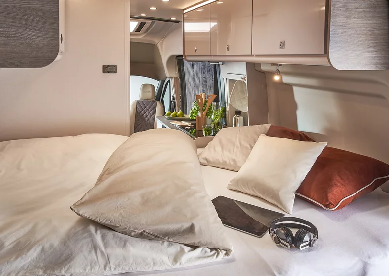 Innenansicht eines Lineo Campervans mit einem gemütlichen Bett, Kissen und einem Tablet.