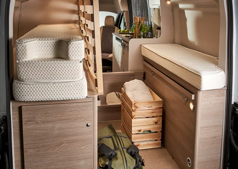 Innenraum eines Wohnmobils mit Matratzen, Holzkisten und Küchenbereich.
