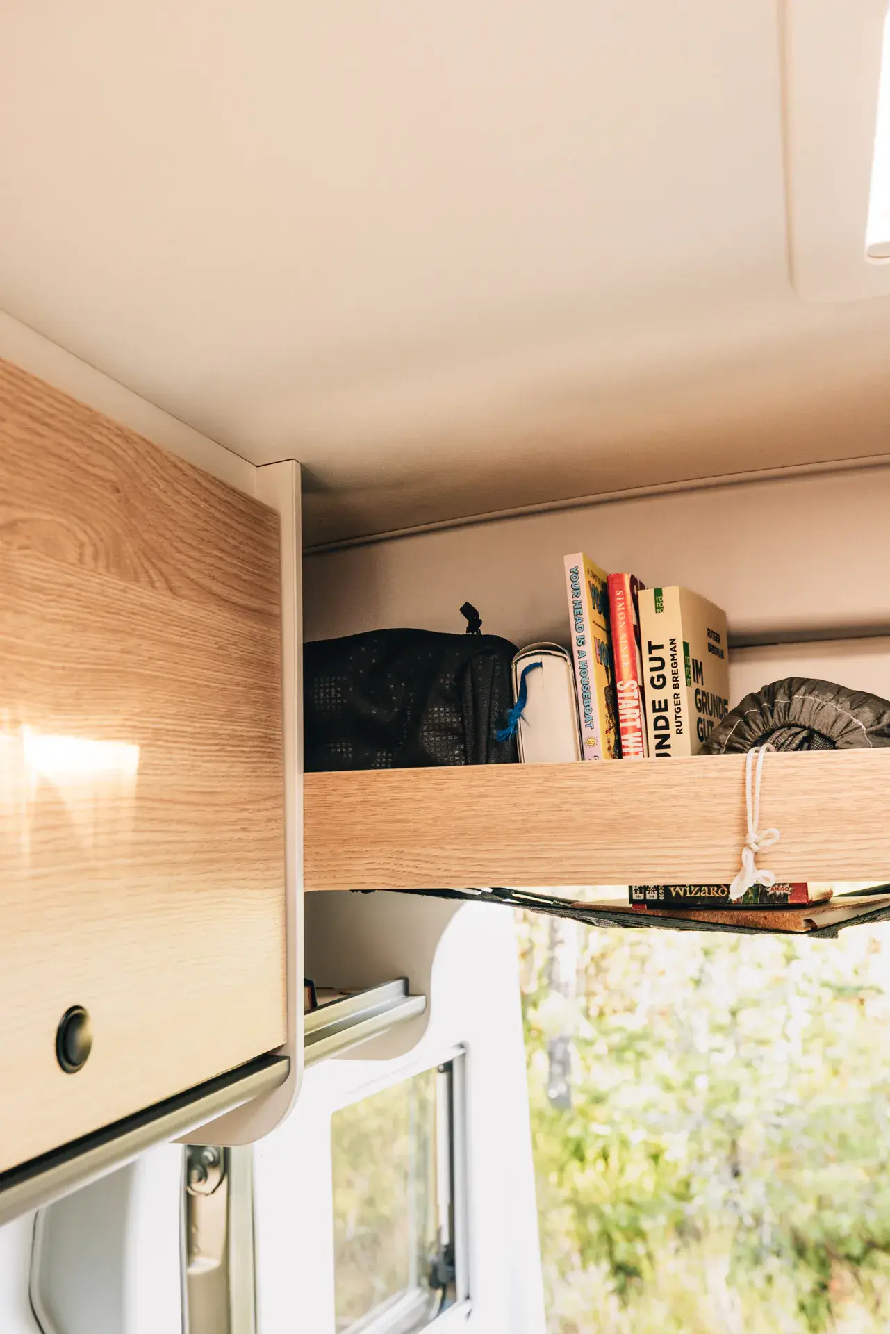 Oberes Regal in einem Sunlight-Camper mit Büchern und Taschen.