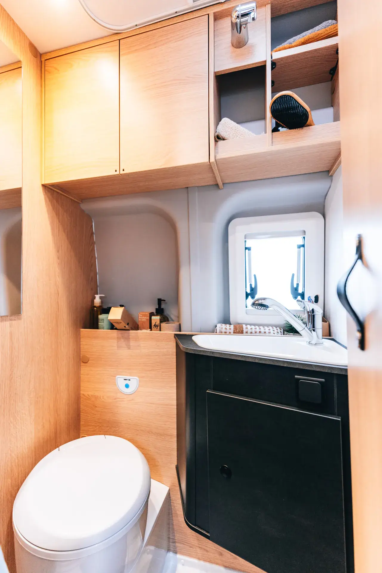 Wohnmobil-Badezimmer mit Toilette, Waschbecken und Holzschränken.